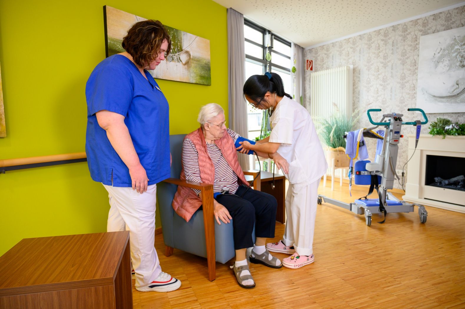 Eine Pflegeschülerin misst bei einer Bewohnerin unter Anleitung den Blutdruck