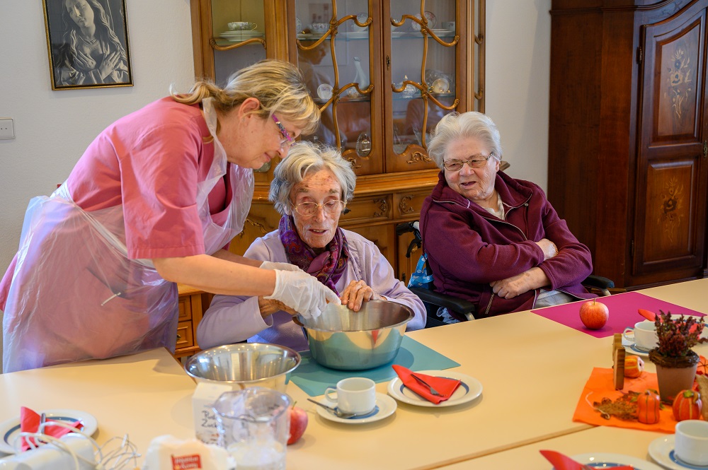 Eine Pflegerin hilft einer Bewohnerin beim Ei-Aufschlagen