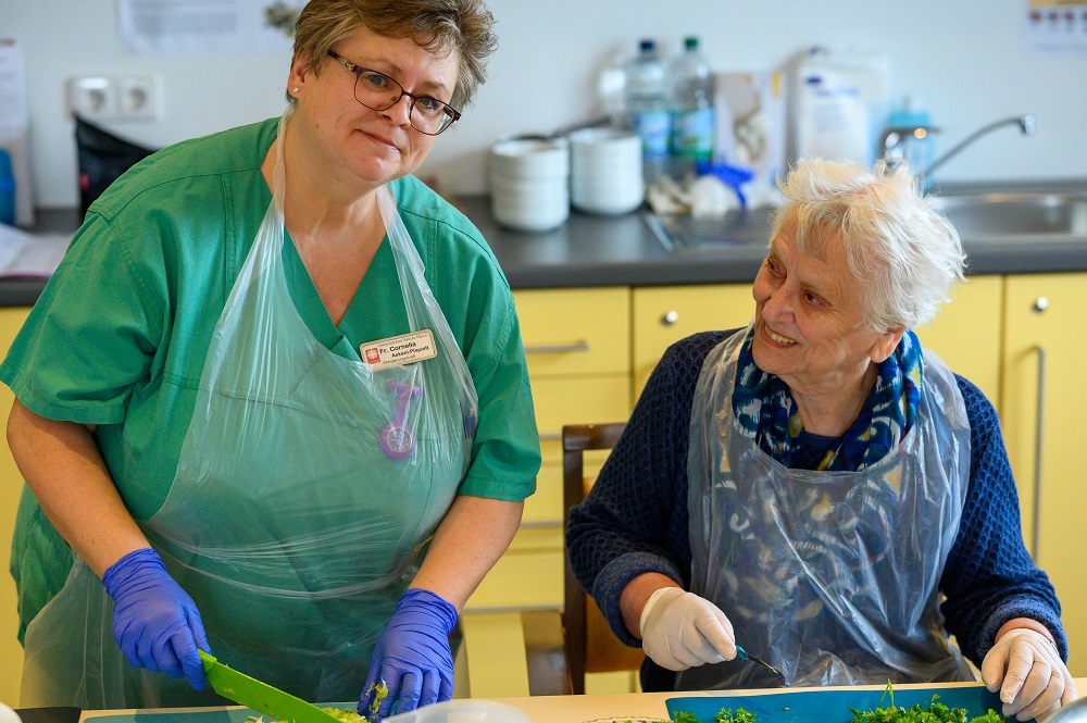 Eine Pflegerin und eine Bewohnerin schnippeln Gemüse