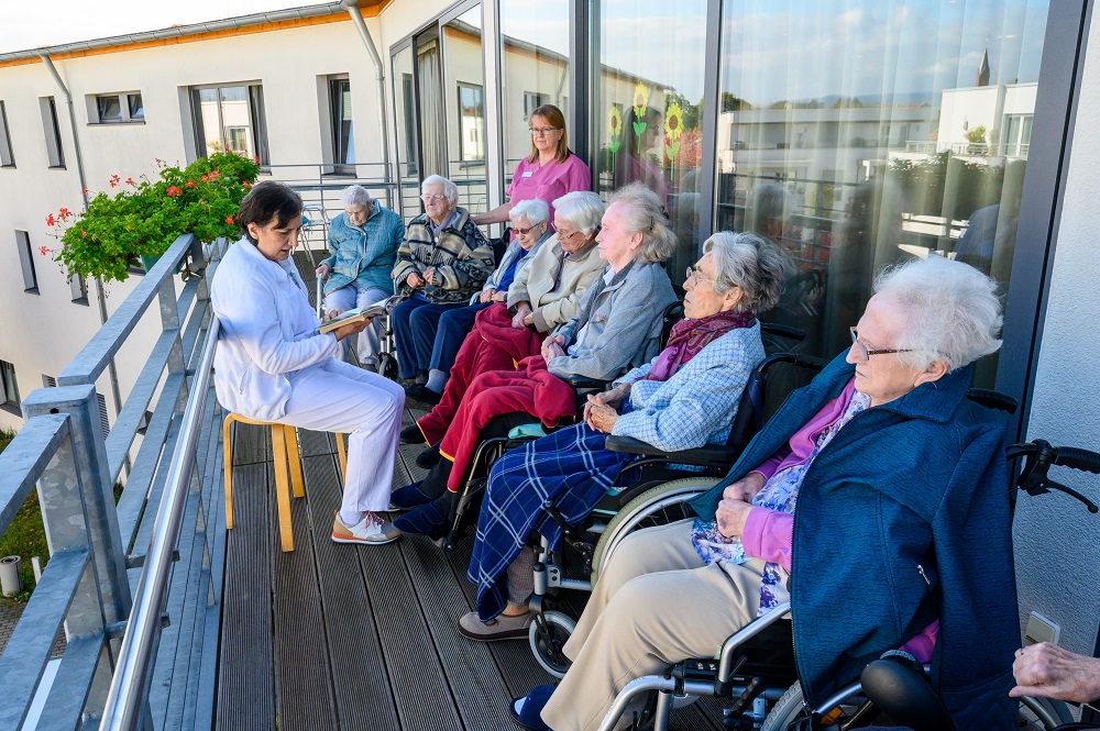 Bewohnerinnen sitzen auf dem Balkon und bekommen vorgelesen